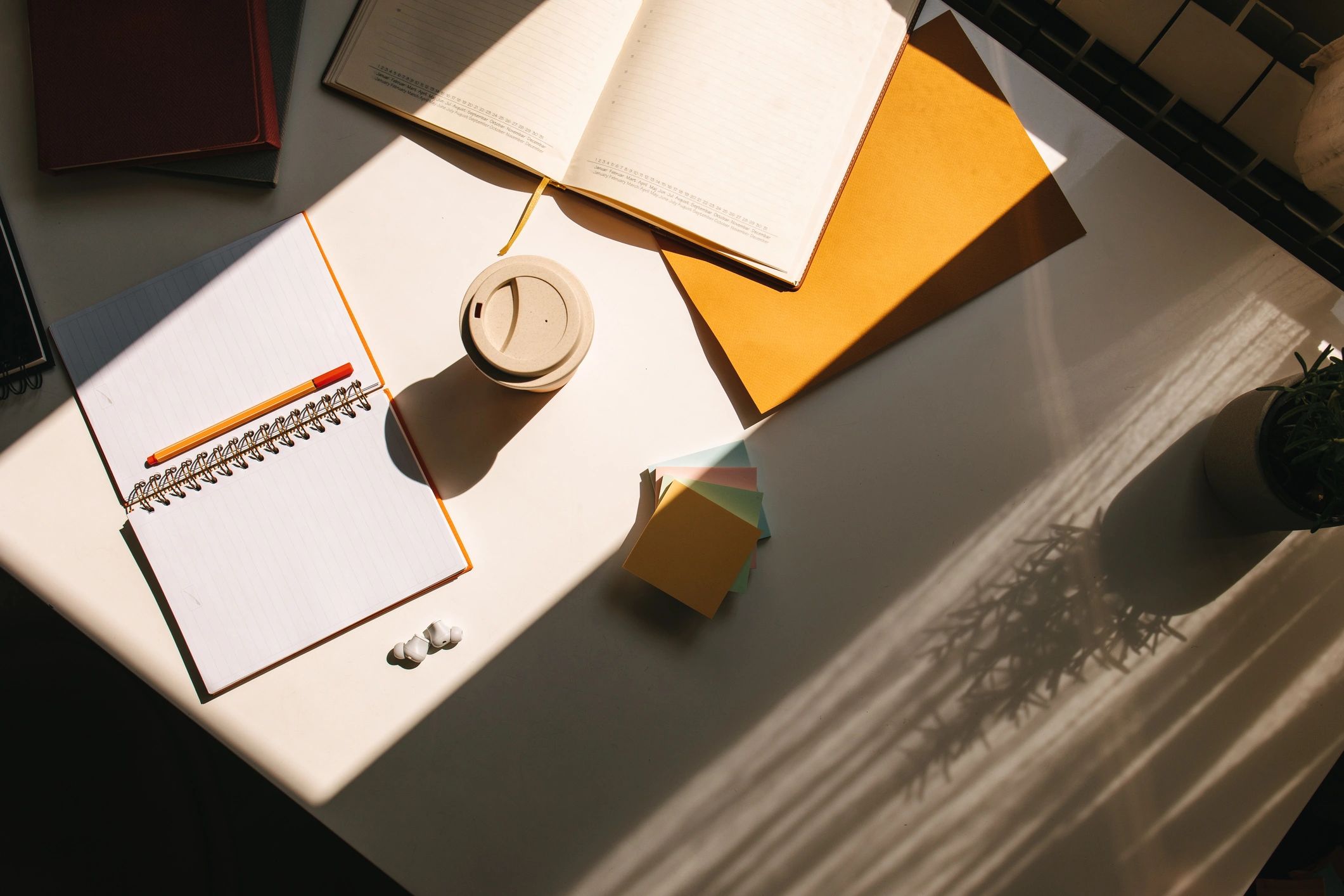 Top view of a desk with an open notebook, coffee, and plant in daylight